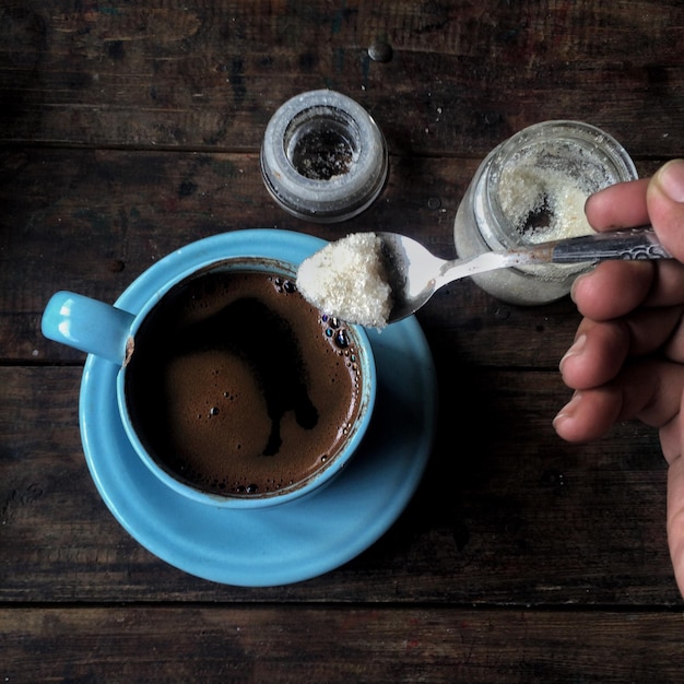 Photo cropped hand of person adding sugar in black coffee at table