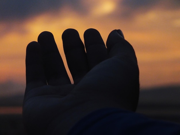 Photo cropped hand of person against sky during sunset