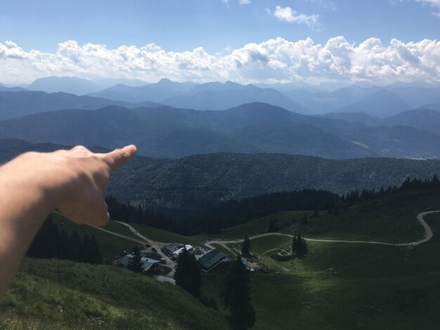 Foto mano tagliata di una persona che fa un gesto alla catena montuosa contro il cielo