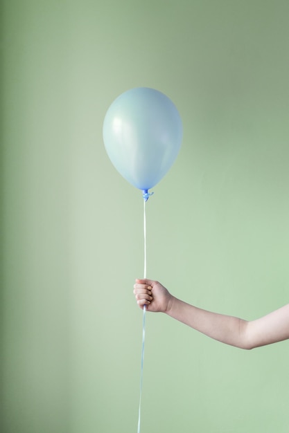 Photo cropped hand of person holding balloon against green wall