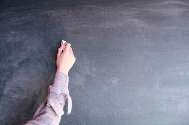 Photo cropped hand of person holding chalk by blackboard