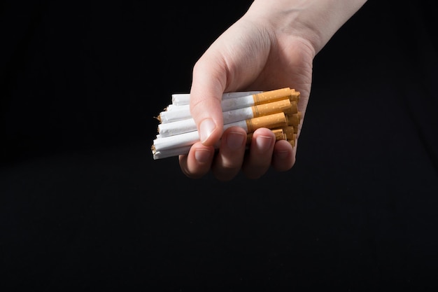 Cropped hand of person holding cigarettes over black background