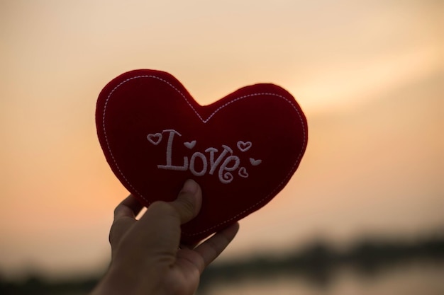 Photo cropped hand of person holding heart shape with text against sky during sunset