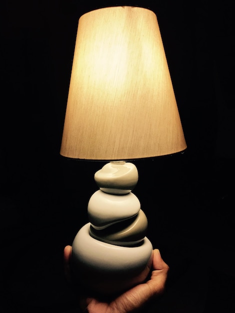 Cropped hand of person holding illuminated lamp in darkroom