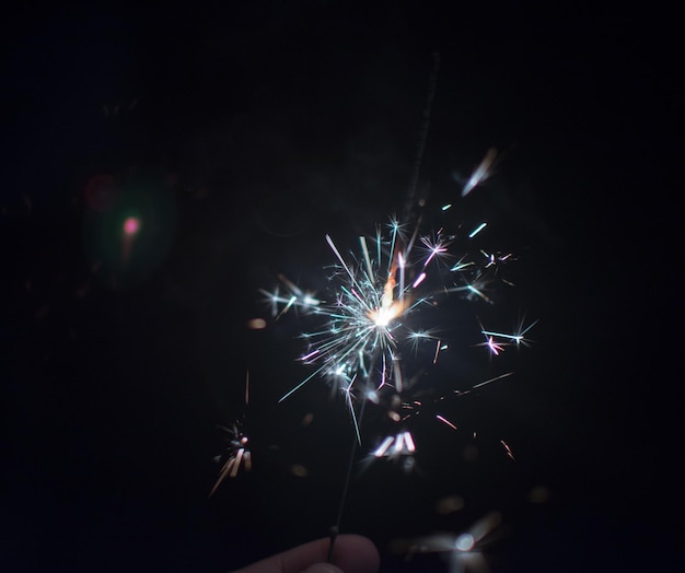cropped hand of person holding illuminated sparkler at night