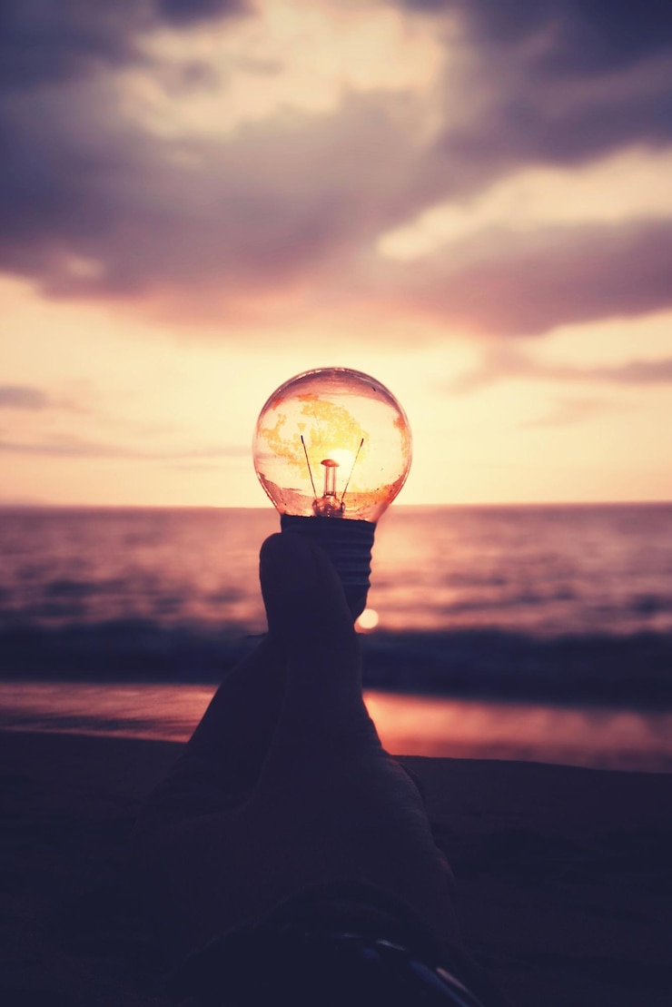Photo 夕暮れの空に照らされたビーチで電球を握っている人の手を切り取った