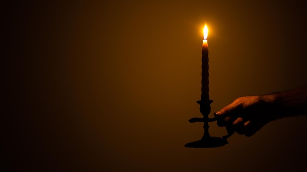 Photo cropped hand of person holding lit candle in darkroom