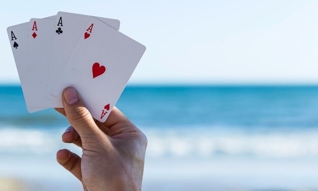 Foto mano tagliata di una persona che tiene le carte da gioco sulla spiaggia contro il cielo