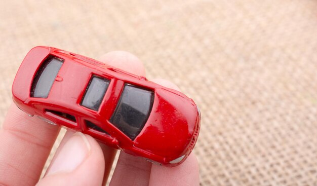 Cropped hand of person holding red toy car on burlap