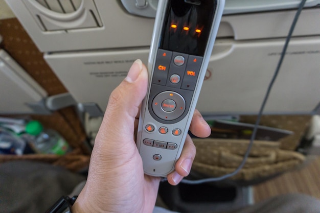 Photo cropped hand of person holding remote control in airplane