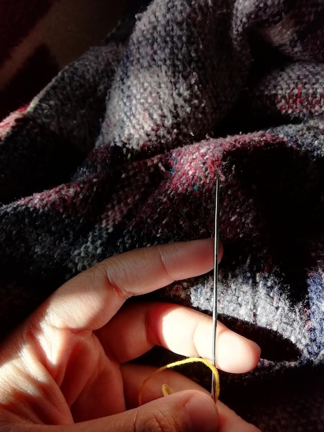 Cropped hand of person holding sewing needle against textile