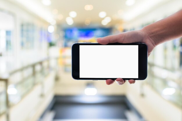 Foto mano tagliata di una persona che tiene uno smartphone in un centro commerciale illuminato