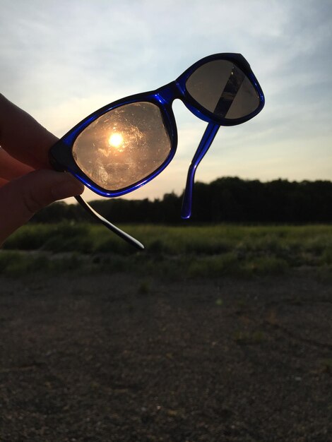 Foto mano tagliata di una persona che tiene gli occhiali da sole contro il cielo