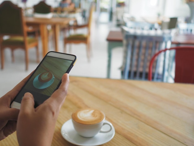 Cropped hand of person photographing coffee through mobile phone on table
