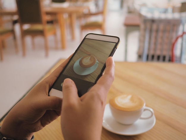 Photo cropped hand of person photographing coffee through mobile phone on table