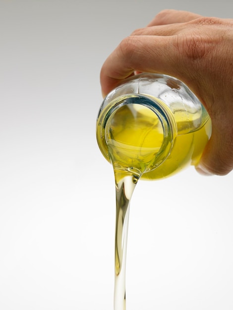 Cropped hand of person pouring oil over white background