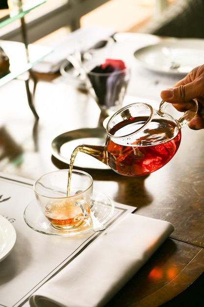 Photo cropped hand of person pouring tea in cup from pot