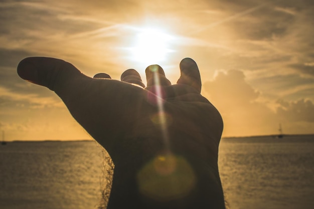 Photo cropped hand of person over sea against sky