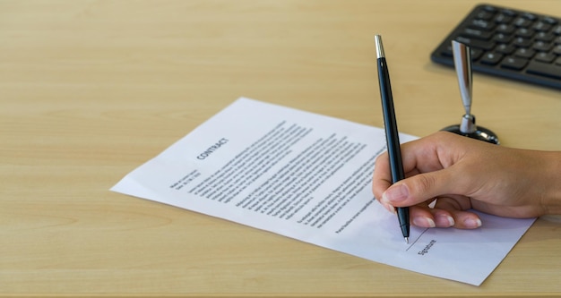 Cropped hand of person signing contract at table