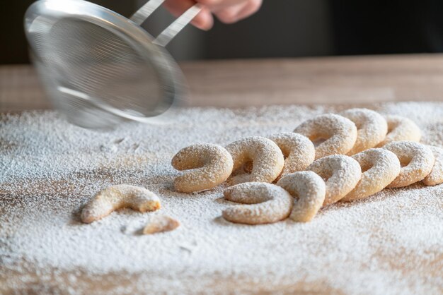 Foto mano tagliata di persona che spruzza zucchero in polvere con un filtro sui biscotti sul tavolo