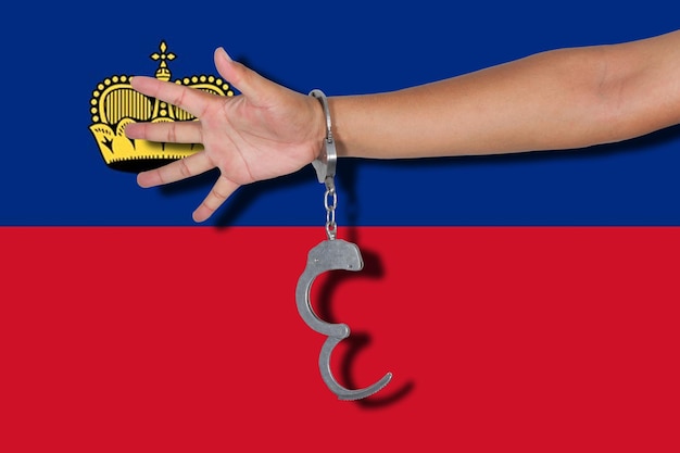 Cropped hand of person wearing handcuffs against liechtenstein flag