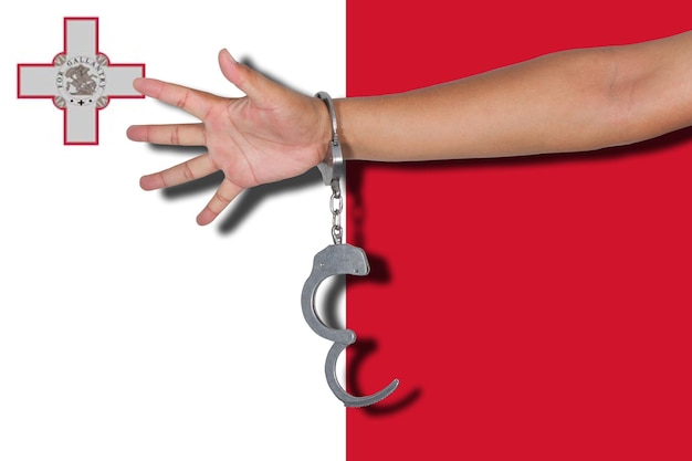 Обрезанная рука человека, носящего наручники на флаге Мальты