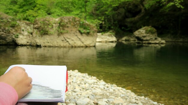 Foto mano tagliata di una persona con un libro al lago