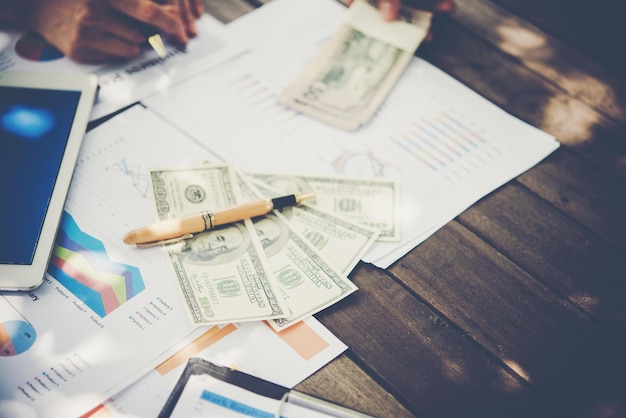 cropped hand of person with charts and paper currencies on table