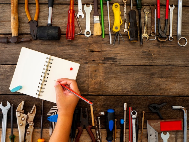 Photo cropped hand of person writing in spiral notebook by hand tools on table