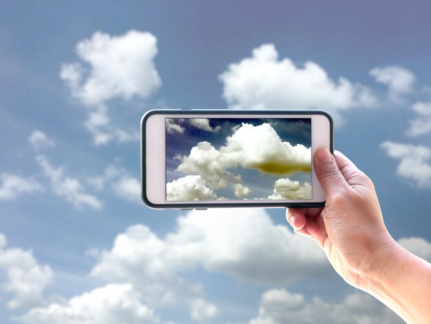 携帯電話で雲の空を撮影する手を切り取った
