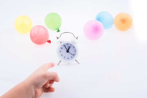 Foto mano tagliata che indica l'orologio e palloncini colorati su sfondo bianco