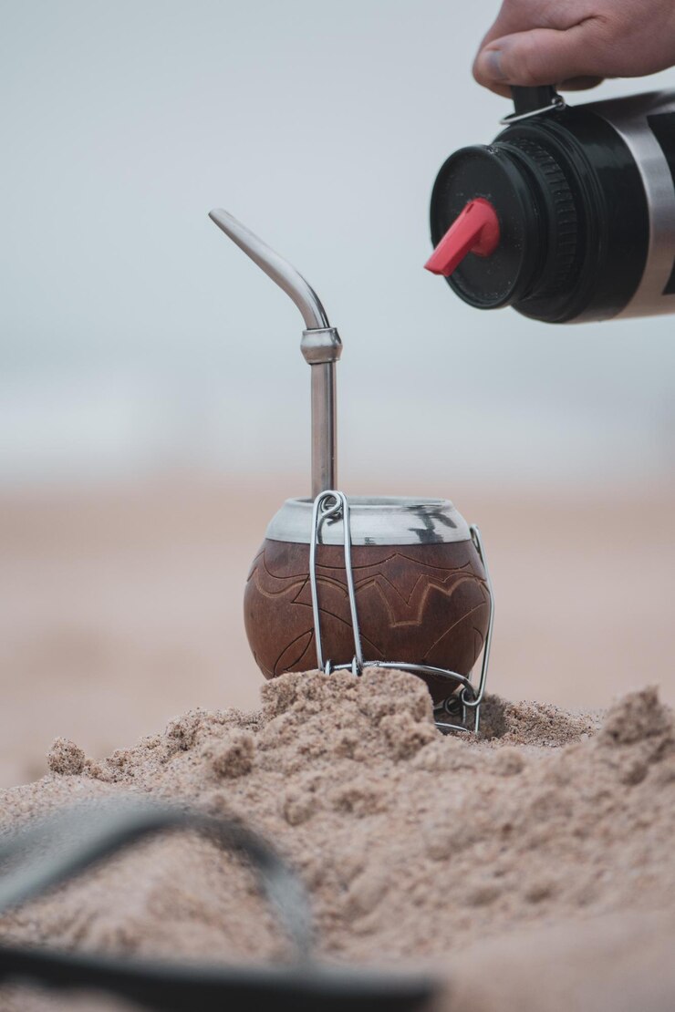 Photo cropped hand pouring drink in container on sand at beach
