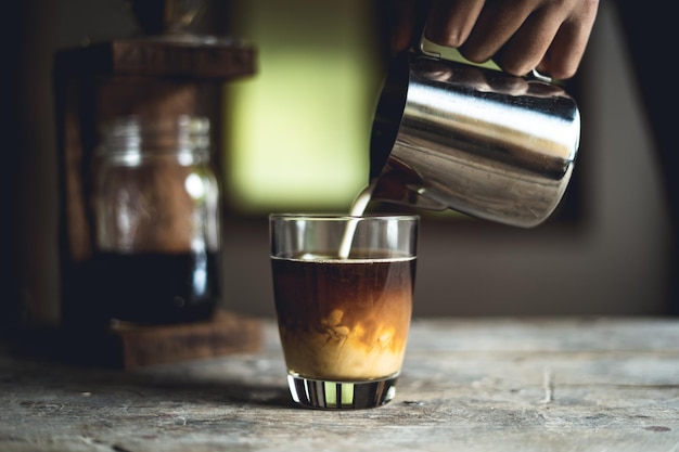 テーブルの上のコーヒーにミルクを注ぐ手を切り取った