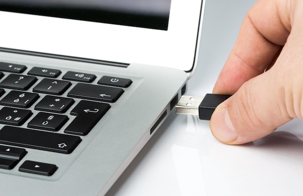 テーブルでラップトップにUSBスチックを入れる手を切り取った