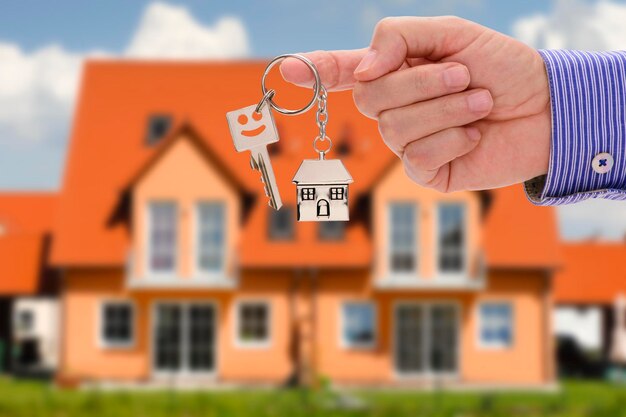 Cropped hand of real estate agent holding key against house