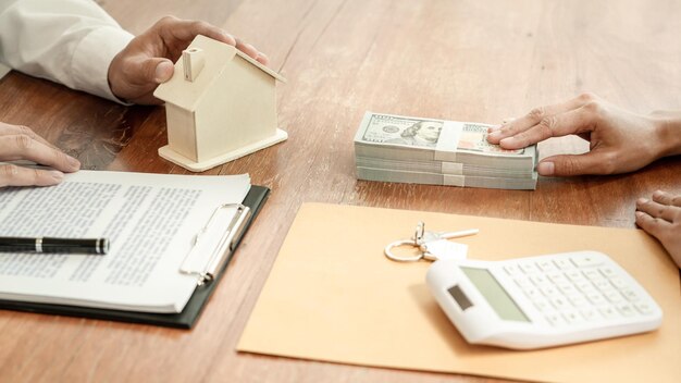 Photo cropped hand of real estate agent holding model home by customer with currency on table