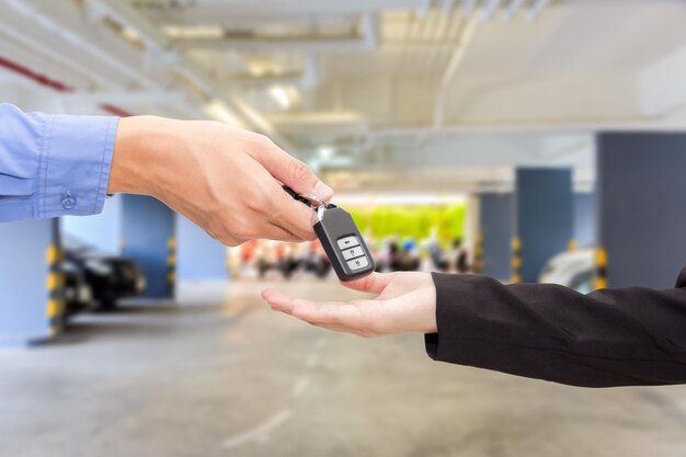 Cropped hand of salesman giving car key to customer in parking lot