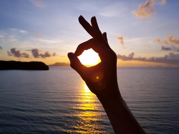 Photo cropped hand showing ok sign at beach during sunset