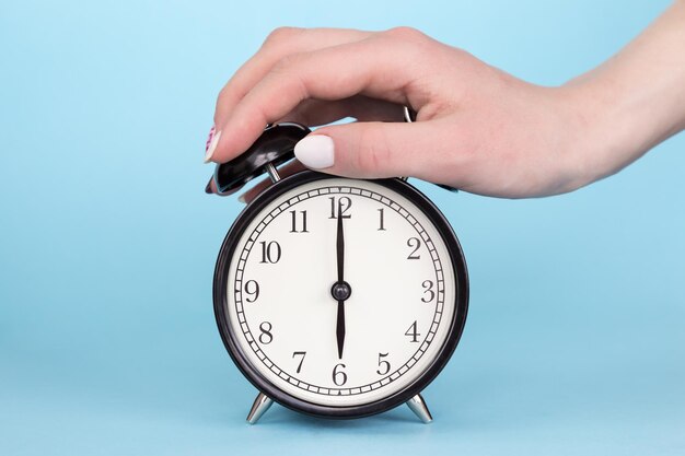 Photo cropped hand snoozing alarm clock against blue background