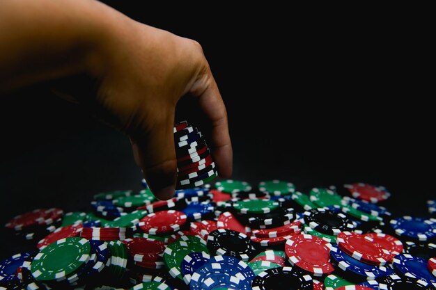 Photo cropped hand spilling gambling chips on black background