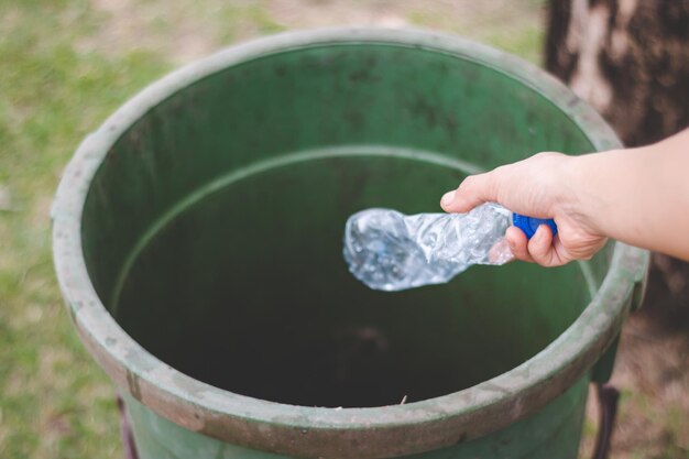 Cropped hand throwing bottle in garbage can