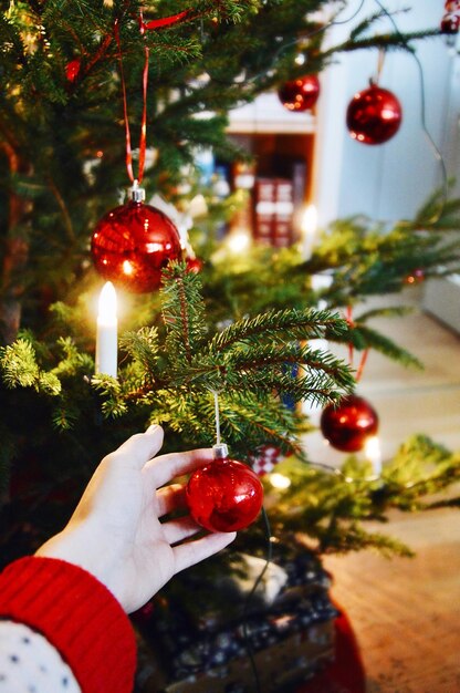 Photo cropped hand touching bauble hanging from christmas tree at home