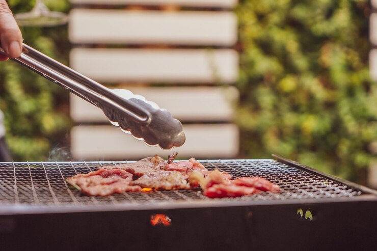 Photo アウトドアパーティーでストーブの上でプレミアムな肉のスライスをグリルするために肉のピンチを使ってカットされた手