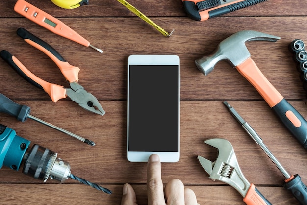 Photo cropped hand using mobile phone by work tools on wooden table