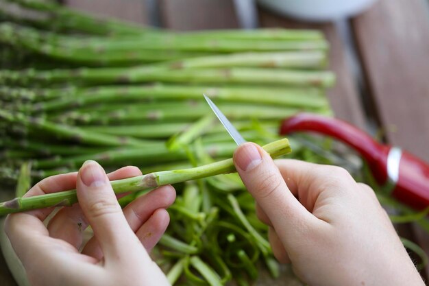 Cropped hand of woman cutting asparagus on table at home