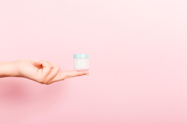 cropped hand of woman holding container against pink background