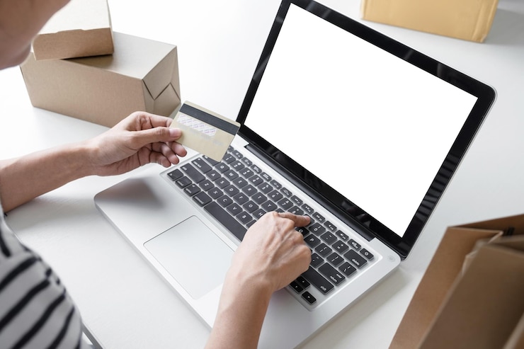 Photo cropped hand of woman holding credit card while using laptop on table