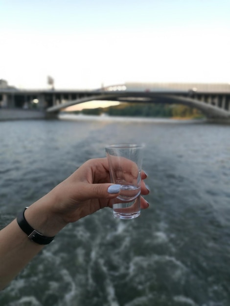 Cropped hand of woman holding drink against river