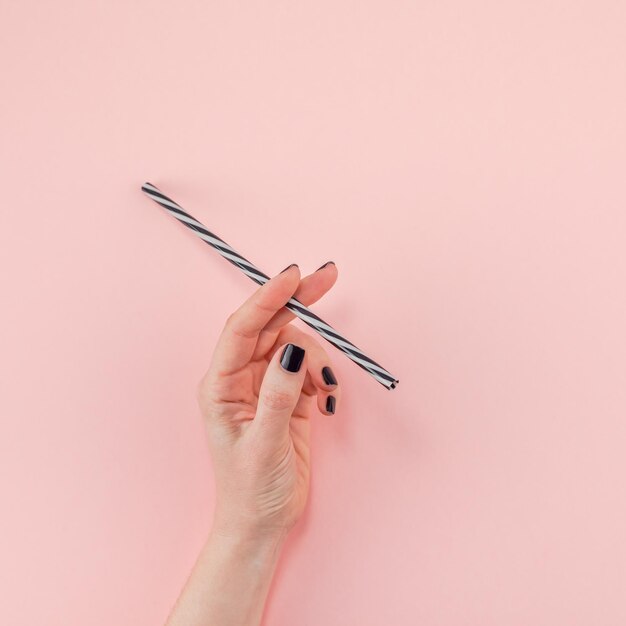 Foto mano tagliata di una donna che tiene una paglia da bere contro uno sfondo rosa