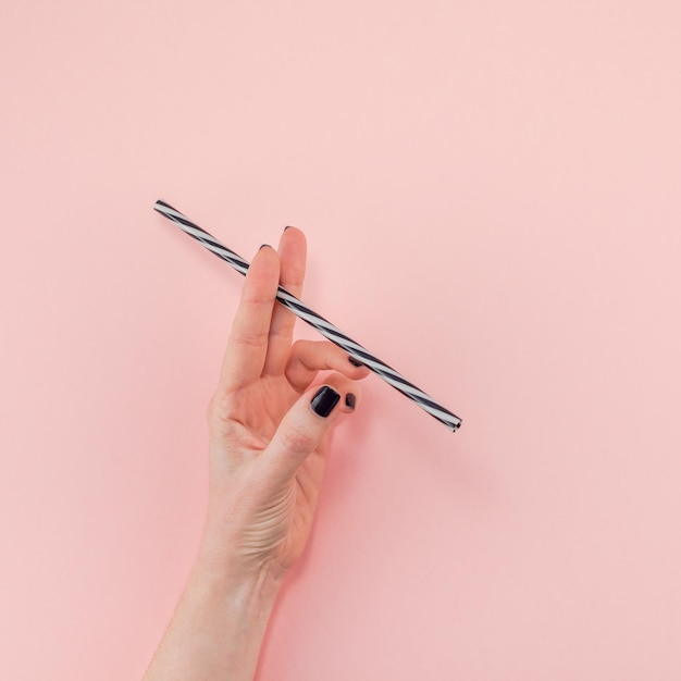 Cropped hand of woman holding drinking straw against pink background